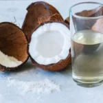 Coconut water in a glass next to two coconut halves.